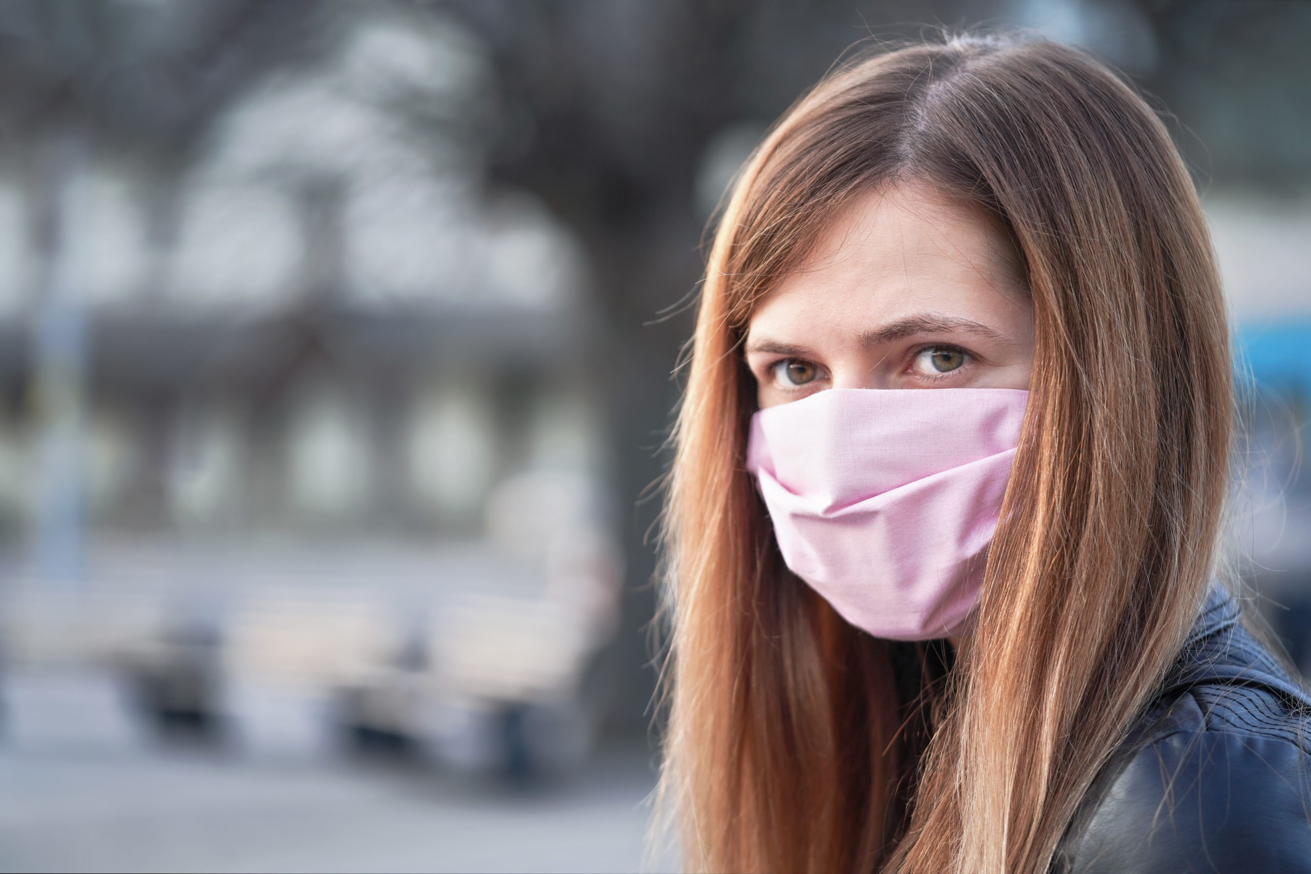 Young woman with hand made face nose mouth mask portrait, blurred empty city square behind her. Can be used during coronavirus covid-19 outbreak prevention